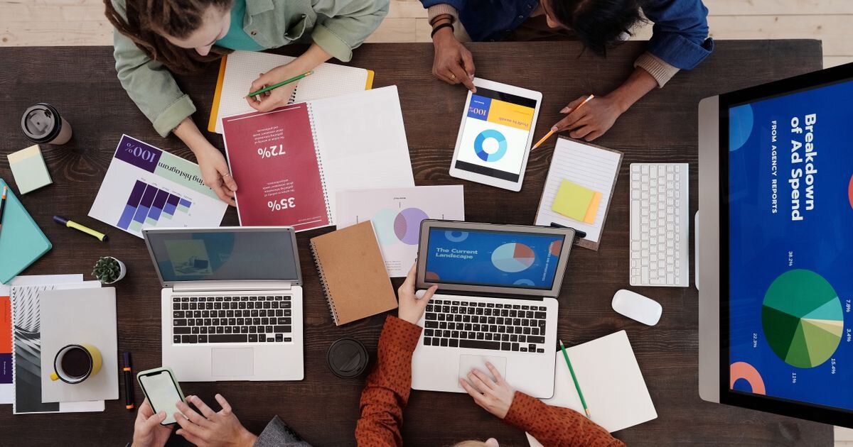 Group of people reviewing pie charts and allocation graphs around a shared desk. Many eyes on one portfolio