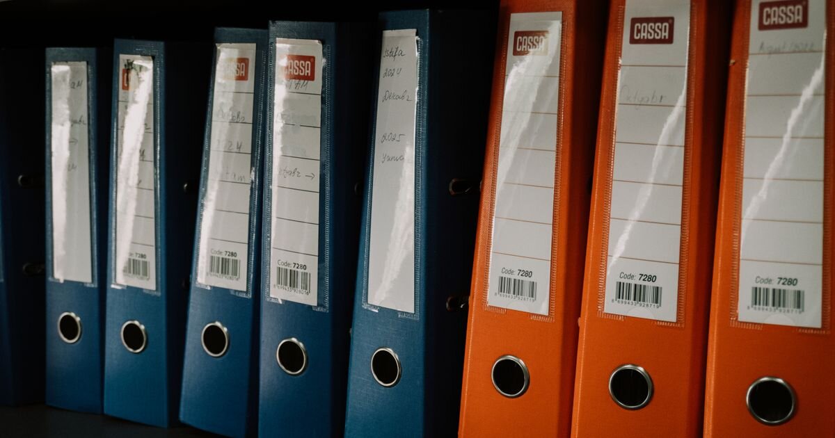 Row of labeled blue and orange binders lined up on a shelf. Separate account records kept side by side